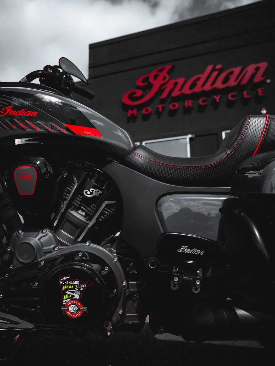 A black Indian motorcycle with a chapter sticker parked outside an Indian Motorcycle dealership